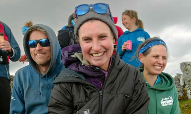 Jamie Aarons at the peak of a munro holding a glass of champagne surrounded by supporters.