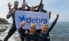 The English Swim challenge team wearing wetsuits, holding a Debra banner as they celebrate with their fists in the air.