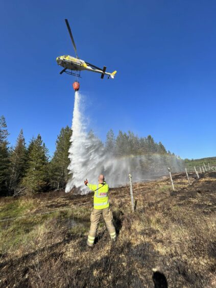 A helicopter water bombs the wildfire in Cannich as a firefighter watches on.