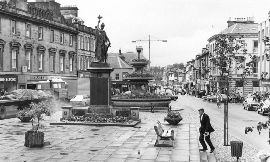 Black and white photo looking down Elgin High Street at war memorial from St Giles Church. 