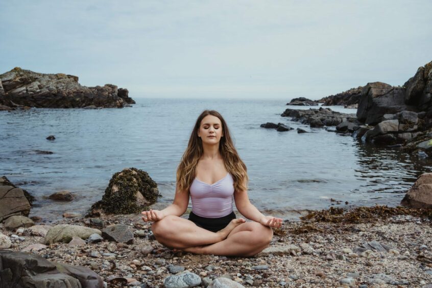 Emma from The Sunshine Movement meditating on a beach with the sea behind her