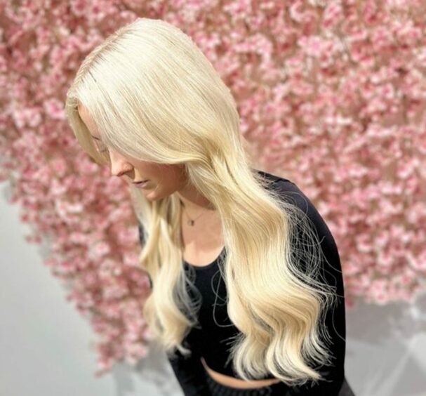 The House of Hair client with newly styled long blonde hair stood in front of a flower wall.