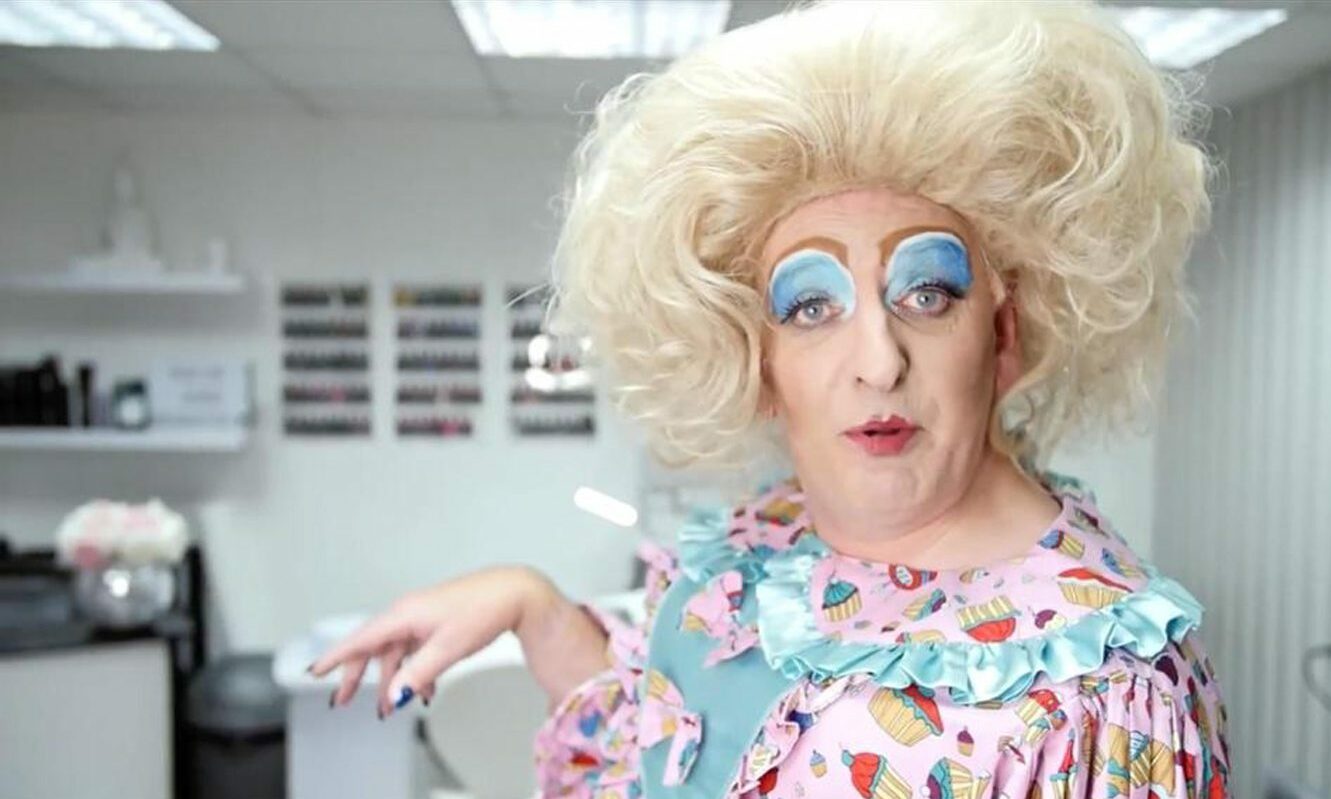 Iain Small dressed in a blonde wig and make-up as a pantomime dame. 