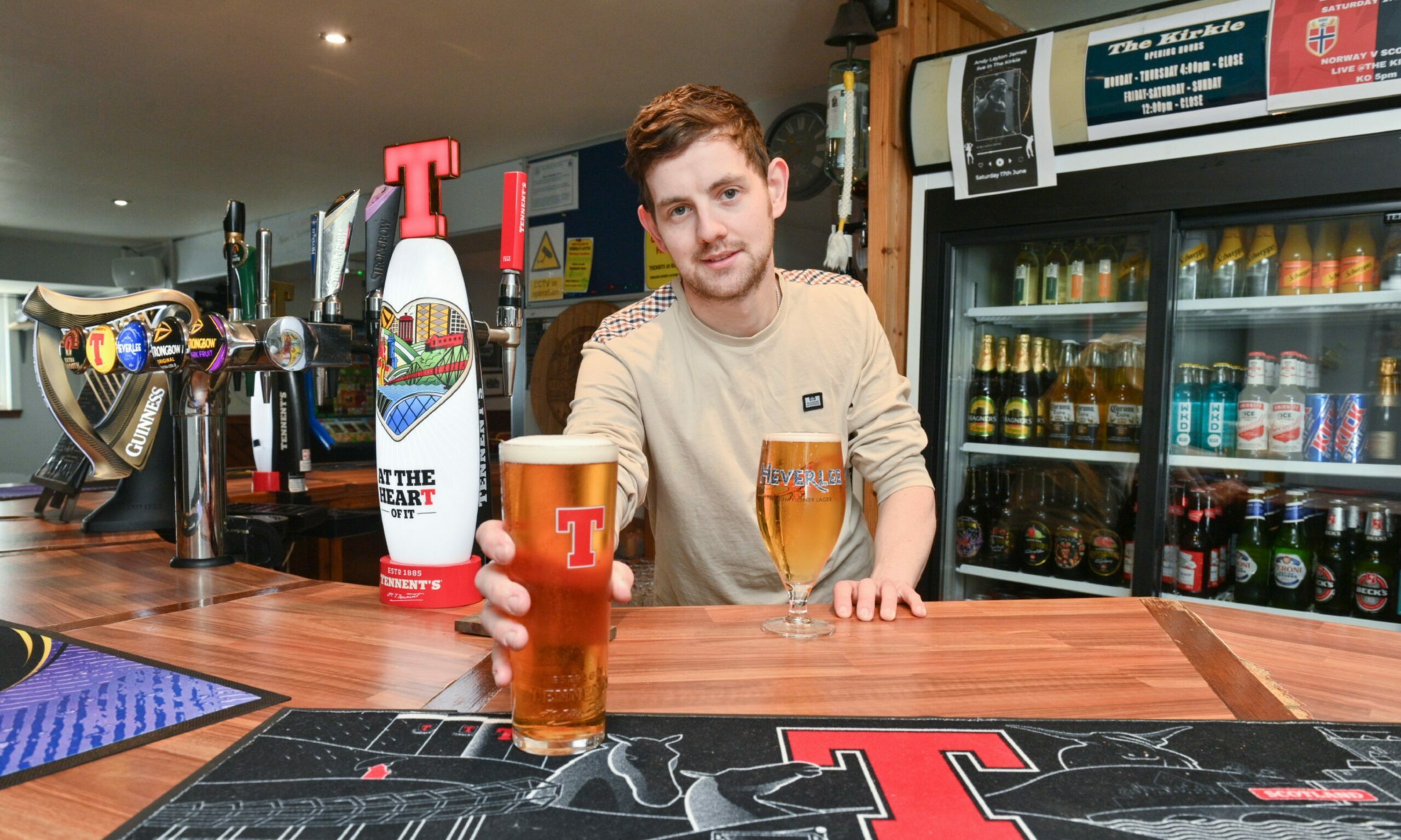 Danny Grant behind the bar at the Kirkie pushing a pint of Tennent's towards the camera. 