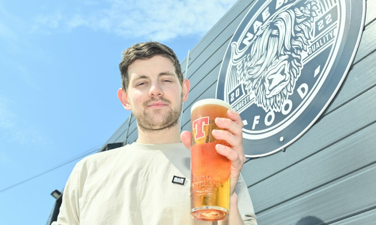 Danny Grant holding a pint of Tennent's in front of the Nae Bad Food food caravan. 