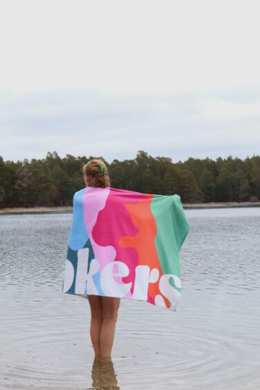 Jo Crane standing in the water with a multicoloured towel with Dookers printed in white letters