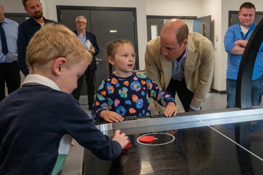 Prince William speaking to a little girl as a young boy plays air hockey.
