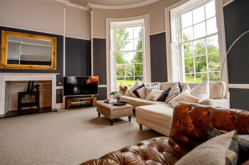 The snug living area with a leather chesterfield sofa, cream L-shaped fabric sofa in front of a fireplace.