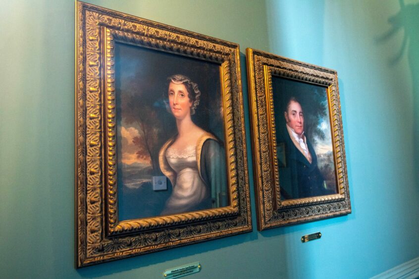 Portraits of Hugh and Elizabeth Gordon in gold frames against a green wall