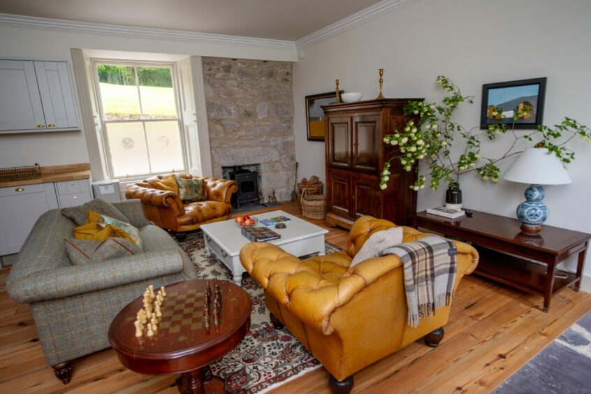 A cosy living area in the House of Horspool, decorated with warm colours, yellow chesterfield arm chairs, a grey plaid sofa, a stone feature wall and a chess table