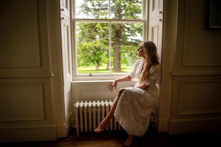 Christina sitting next to a window in the house, looking out at the greenery outside