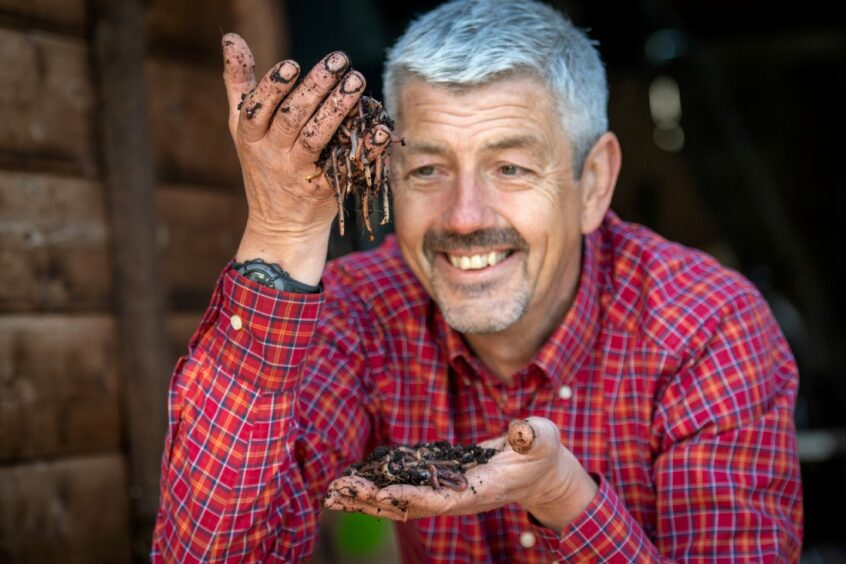 Scott Baxter smiles with worms in his hands.