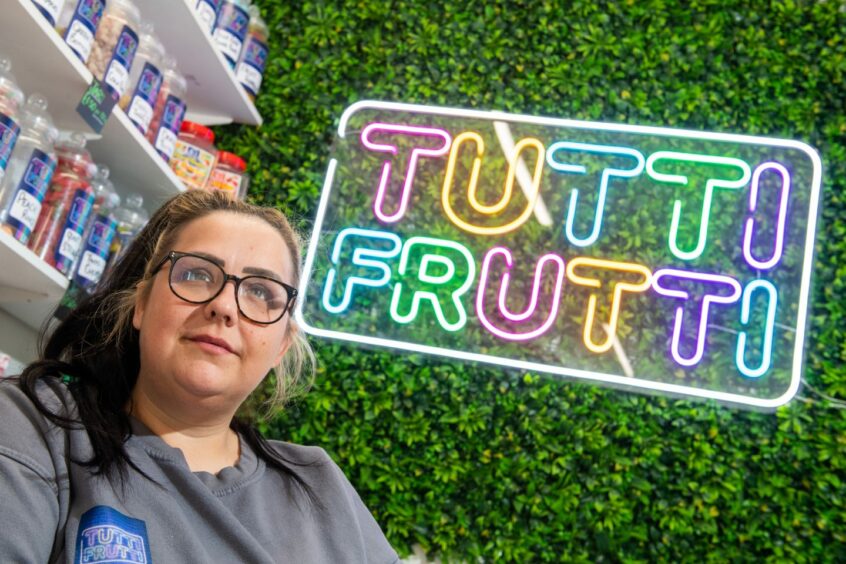 Leanne in front of LED sign that reads 'Tutti Frutti'.
