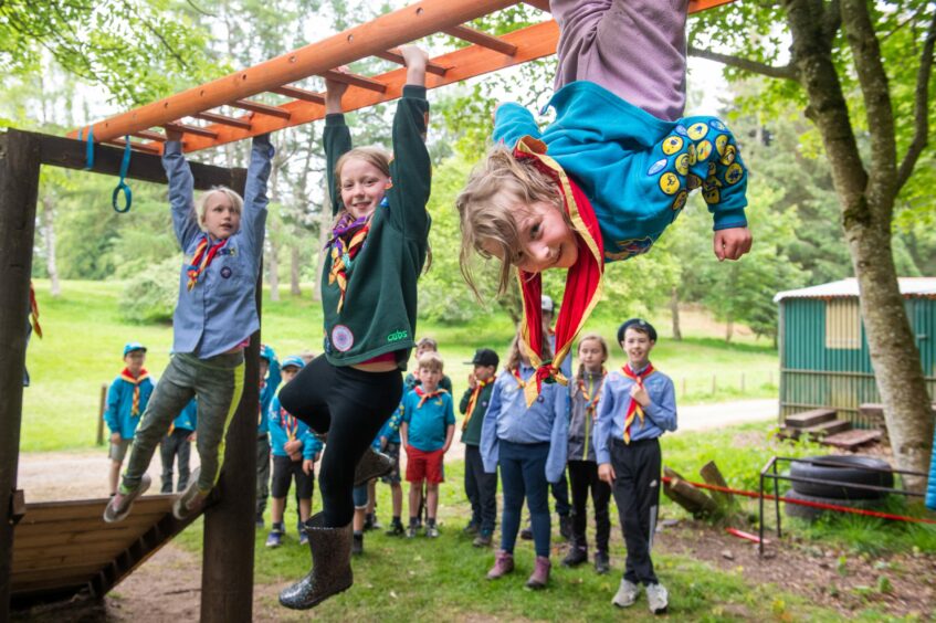 Three children hanging from bars in the obstacle course 