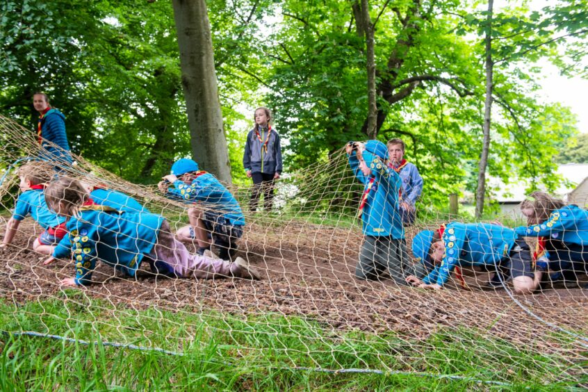 Children crawling under a net as part of the Scouts assault course 