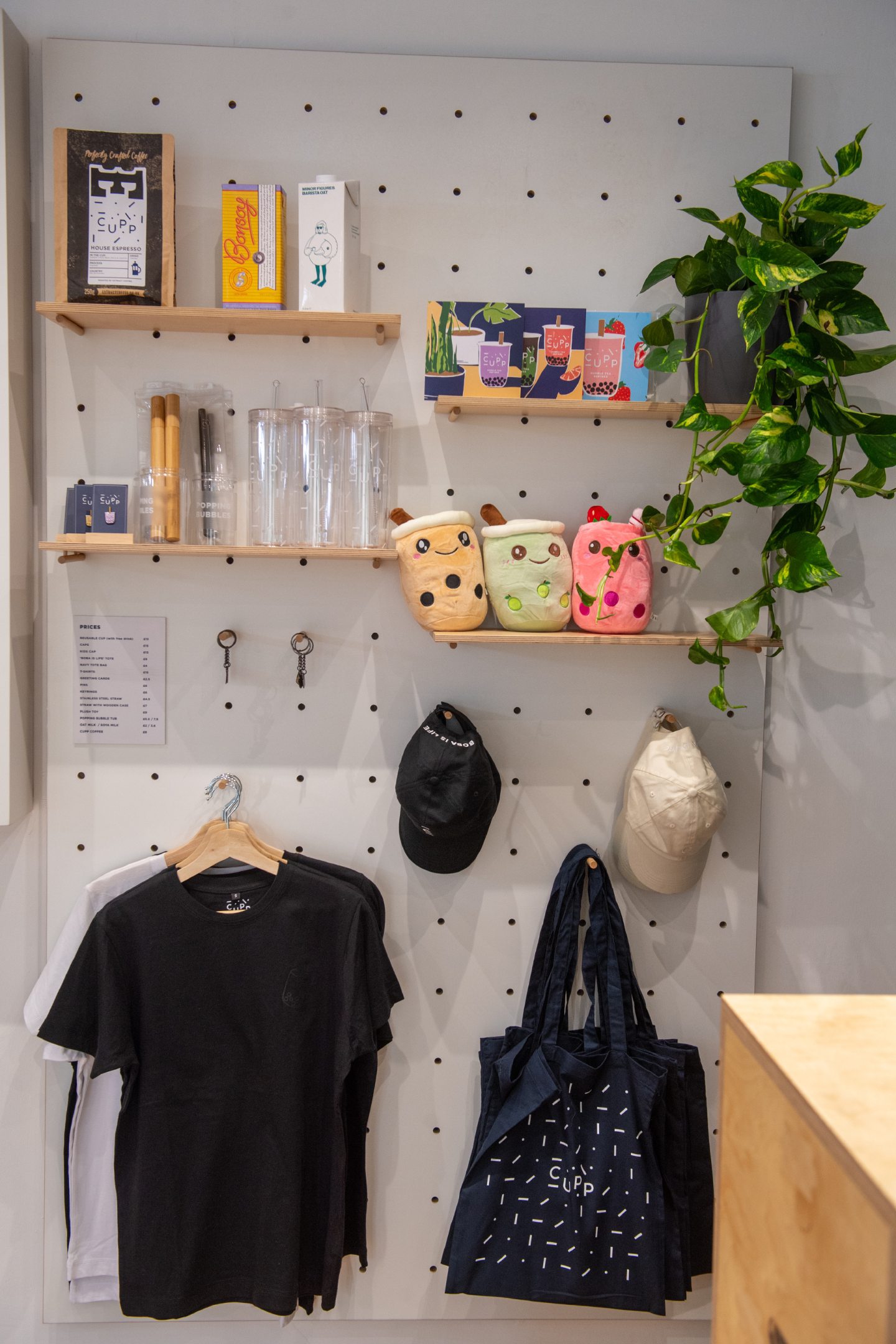 Wall inside shop featuring CUPP Bubble Tea merch including T-shirts, hats and plush toys.