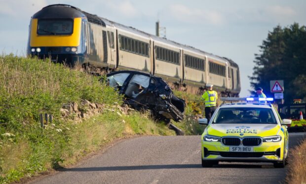 The scene of the crash with a train passing by the vehicle that crashed near the rail line and police at the scene.