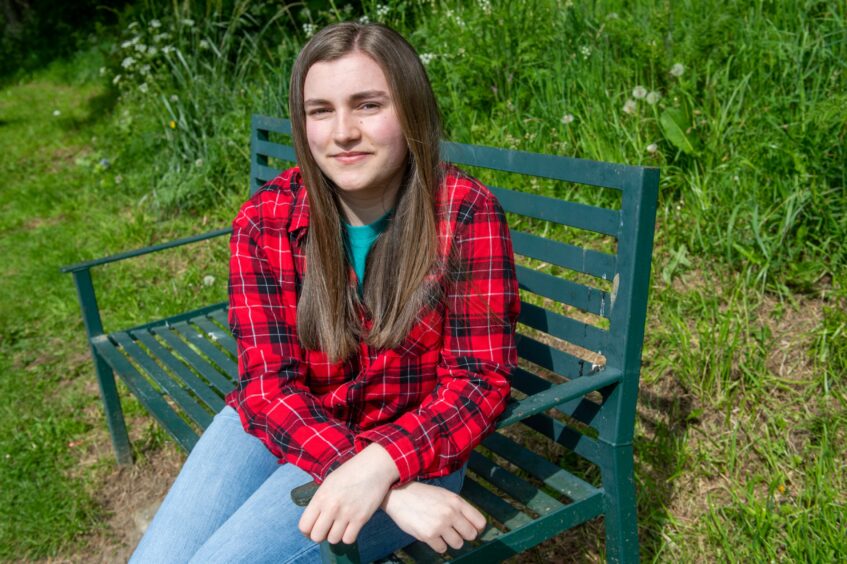 Katie Gibbs sitting on a bench in Inverurie wearing a red checked shirt