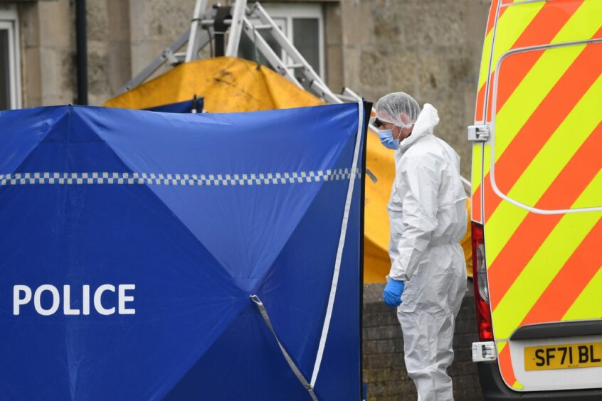 Forensic officers in protective gear next to a van and a blue police tent at the scene of the incident in Fraserburgh