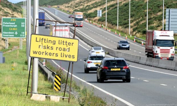 Looking up the hill on AWPR from Stonehaven with traffic on road and sign saying "lifting litter risks road workers lives" at side of road.