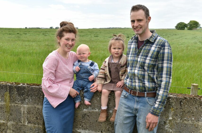 Helen, Wyatt, Willow and Stephen Martyn leaning and sitting on a stone wall with a field of grass behind them