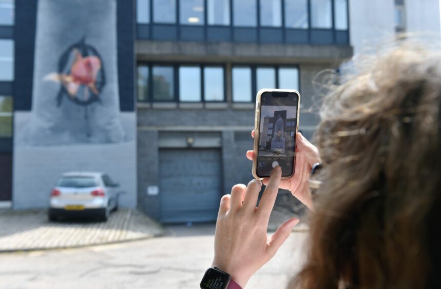 A woman taking a picture of one of the murals on her mobile phone.