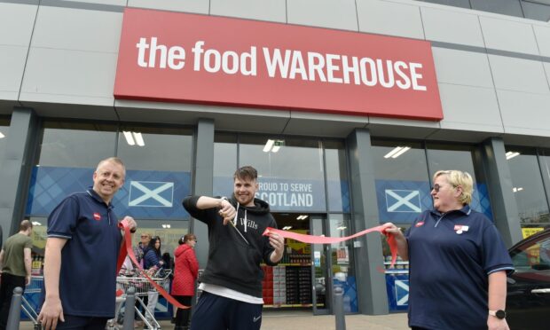The Food Wareshouse staff hold a ribbon outside the door as customer David Finch cuts it with scissors