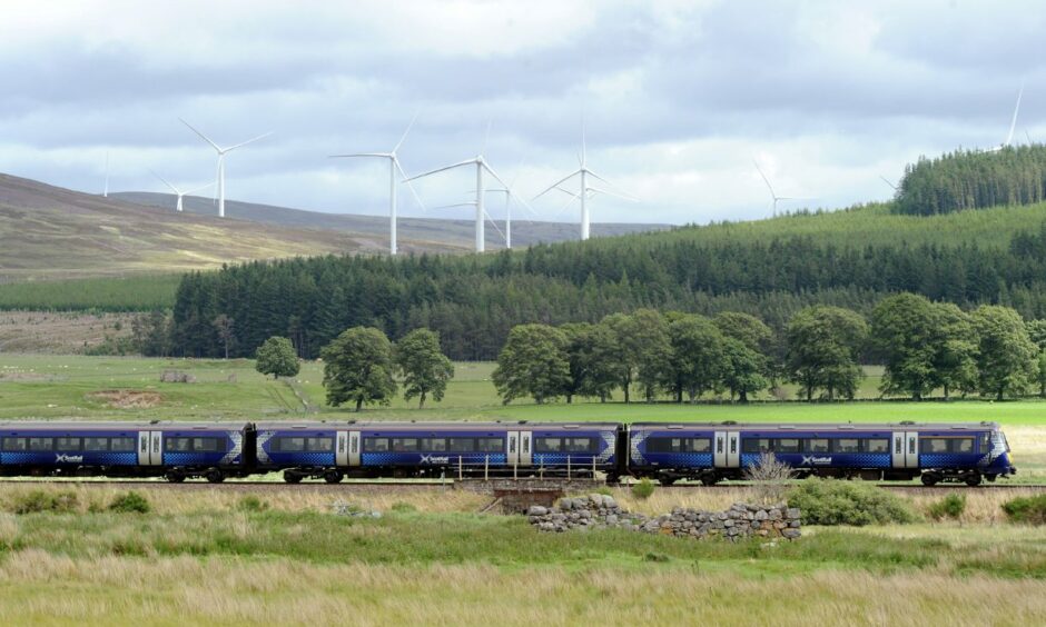 The turbines at Moy Windfarm in the distance as a Scotrail train passes in front.