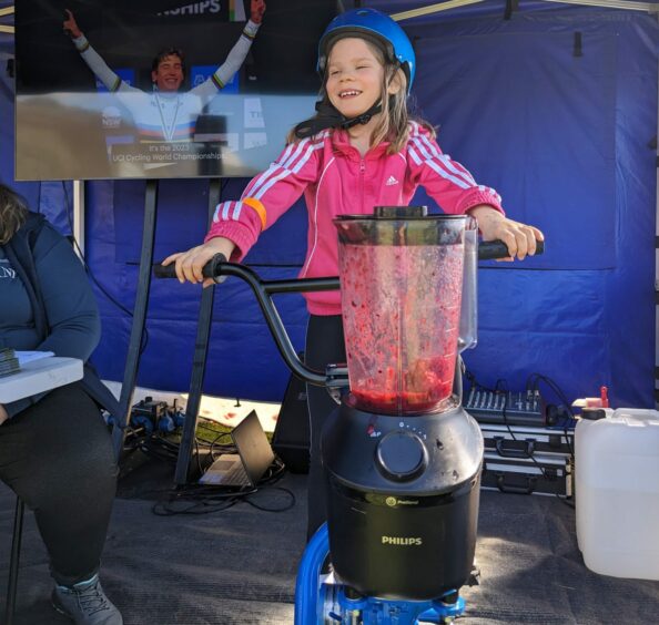 A young girls makes a smoothie using the smoothie bike.