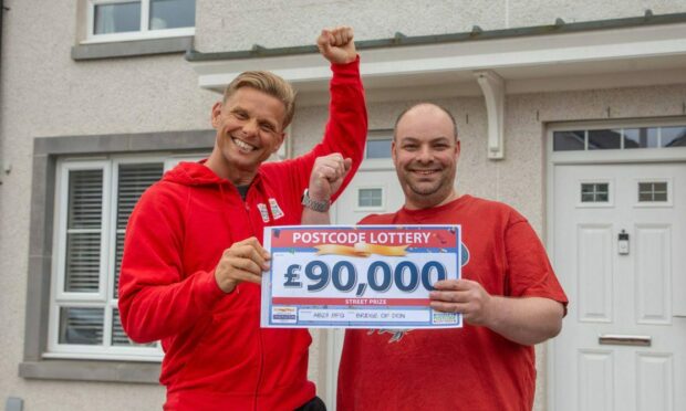 A standing Jeff Brazier hands over a £90,000 People's Postcode Lottery cheque to Craig Stephen who is also standing.