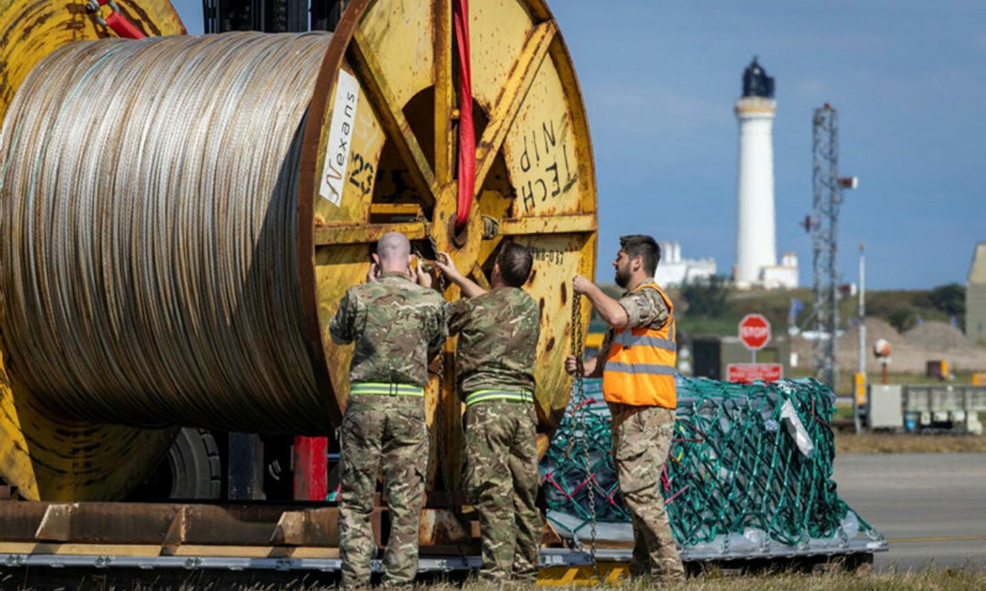 RAF crews inspect cabling with Covesea lighthouse in Lossiemouth in background. 