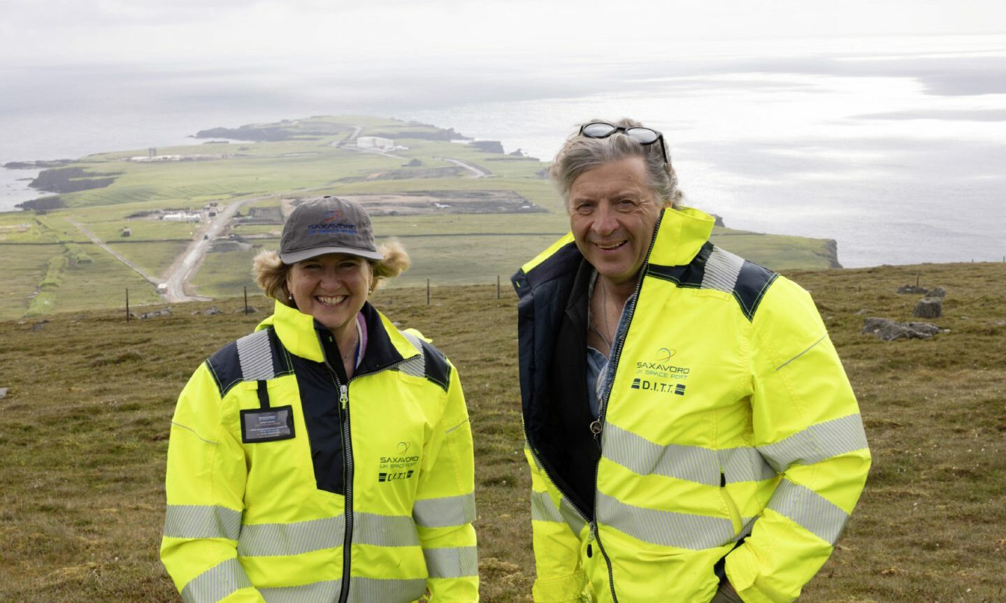 Frank Strang and his wife Debbie wearing high-viz jackets with spaceport behind. 