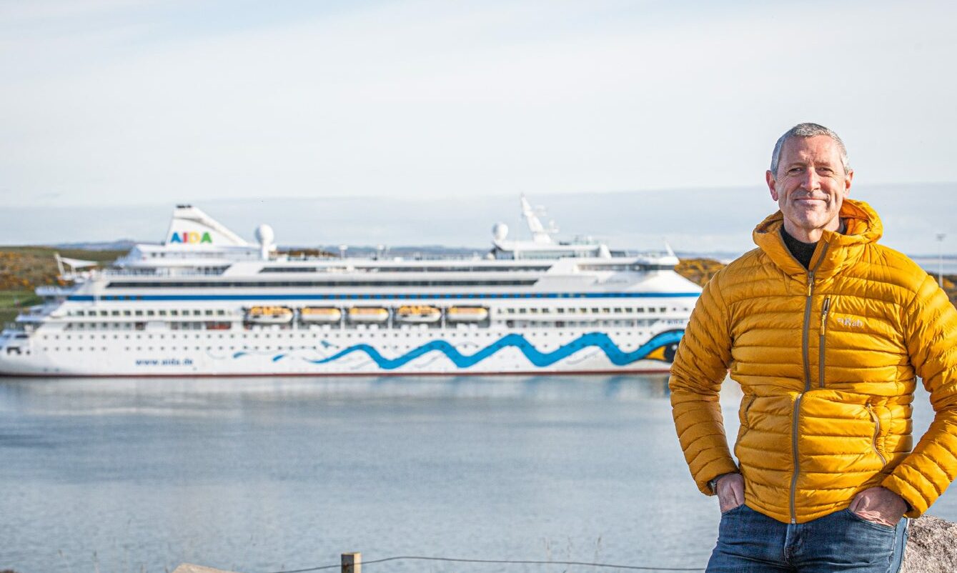 Chris Foy, Chief Executive of Visit Aberdeenshire, standing with a cruise ship behind him