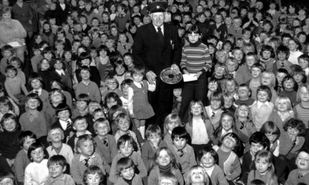 In 1977, Dyce Primary School pupils gathered round to give their janitor, Alex Cheyne, a big send off when he retired. He received gifts from the oldest and youngest pupils, Nicola Reid, left, and Carol Main. Image: DC Thomson