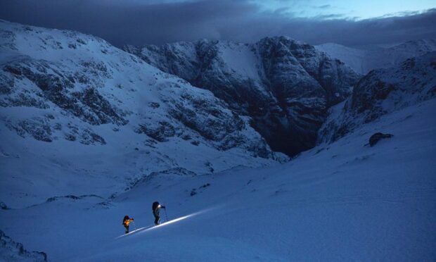 Two mountaineers climbing Glen Coe in the snow by torchlight in the early morning light.