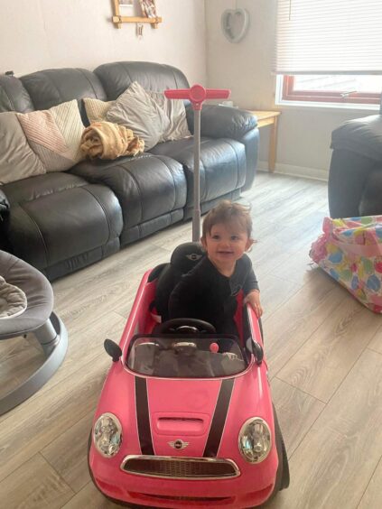 Mia sitting in a pink childrens push car in the family's livingroom