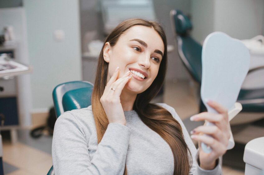 Dental patient sat in dentist's chair looking at newly whitened teeth in a hand held mirror.