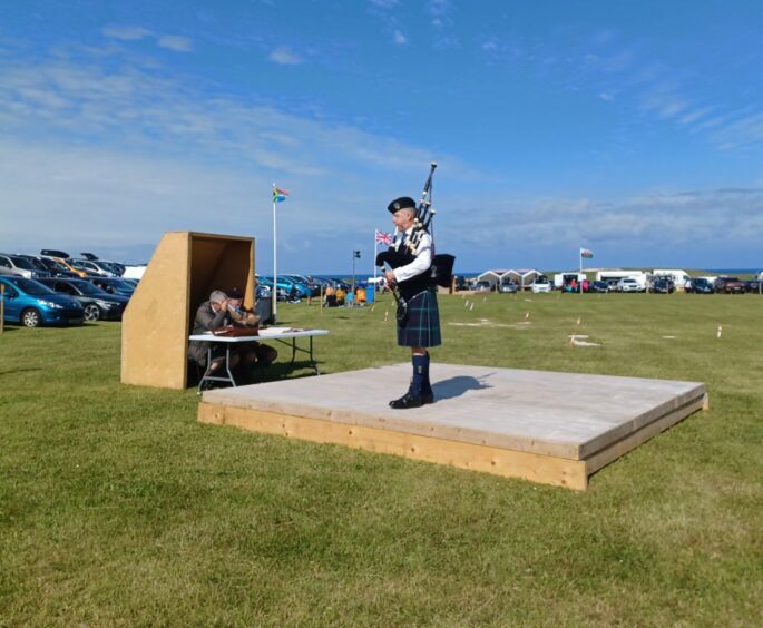 A piper plays on a wooden platform in the middle of a field.
