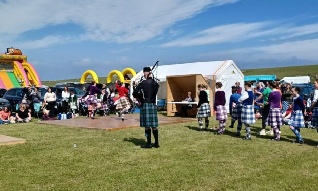 A piper plays for a group of young Highland dancers while others queue behind him.