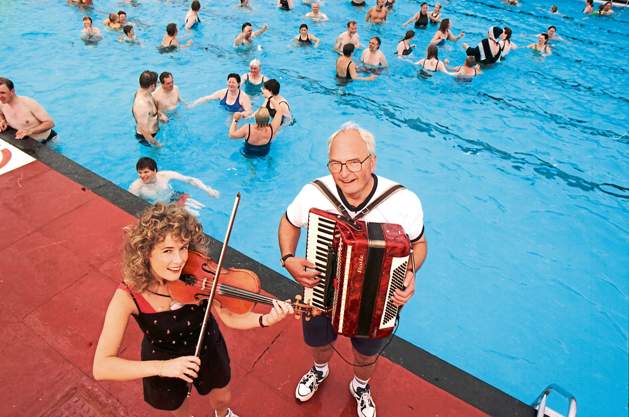 A man with an accordion and a woman with a violin playing poolside at Stonehaven open air pool near Aberdeen in July