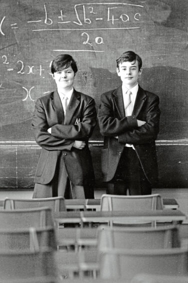 Two pupils standing in front of a black board with their arms folded