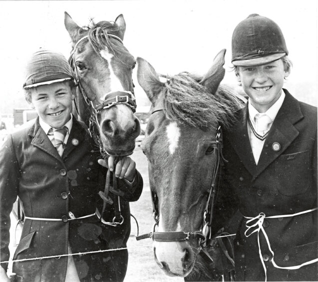Two youngsters posing with horses, wearing horse-riding gear at the Turriff Show