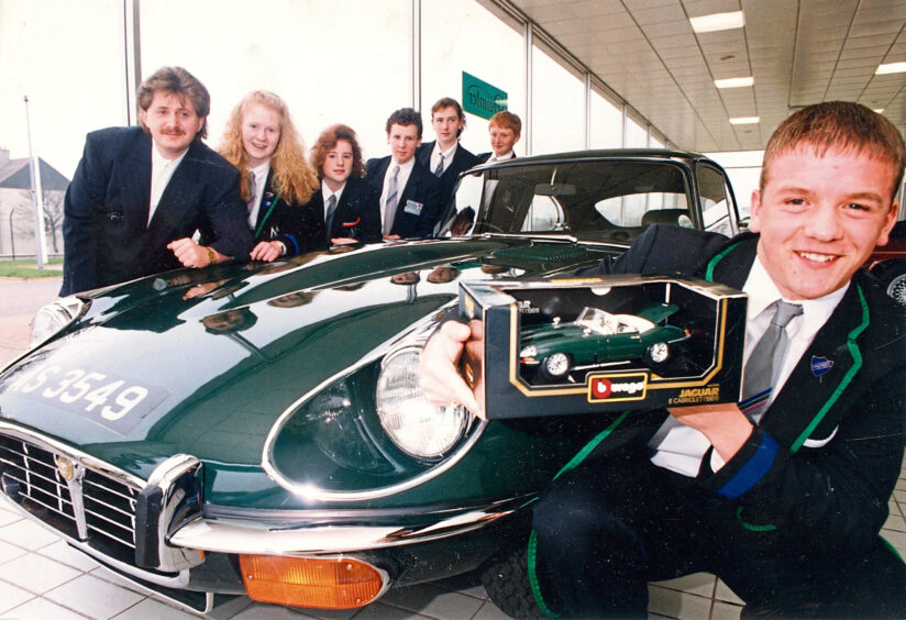 St Machar Academy students with a car. The student at the front is wearing a head boy badge and holding a small model of the car