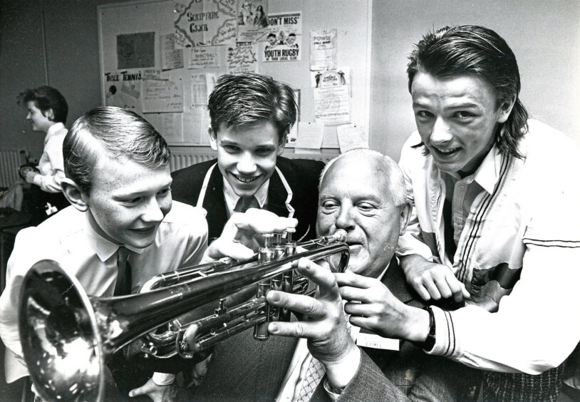 Three pupils with an older man playing a trumpet during a reunion