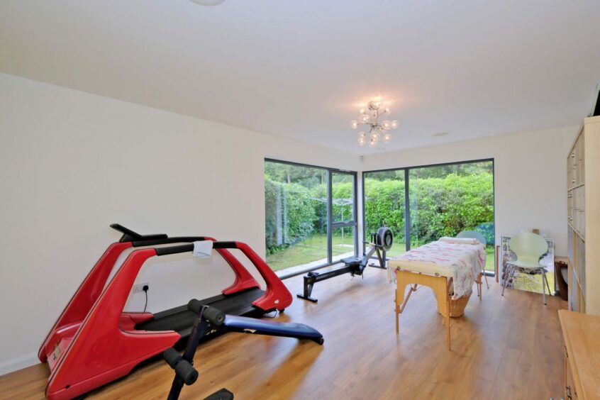 The gym in the home including a rowing machine, treadmill and massage bench. There are two windows looking out into the garden