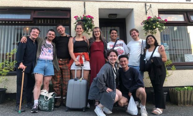 A group of people pose together smiling, some with luggage.