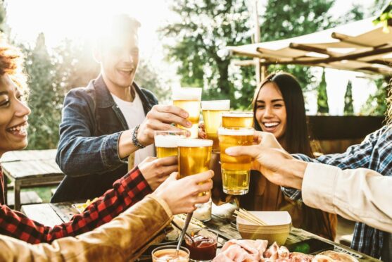 Image of young people cheering with pints of beer. Smiling and the sun is shining.