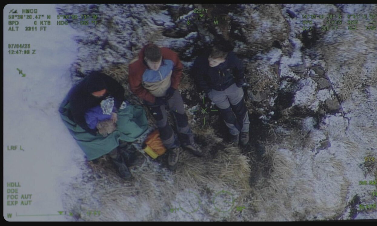 Camera image from helicopter showing Glencoe hillwalker holding dog with two other members of public. 