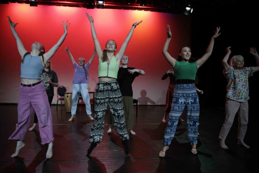 a group of women raise their arms during a dance performance on stage