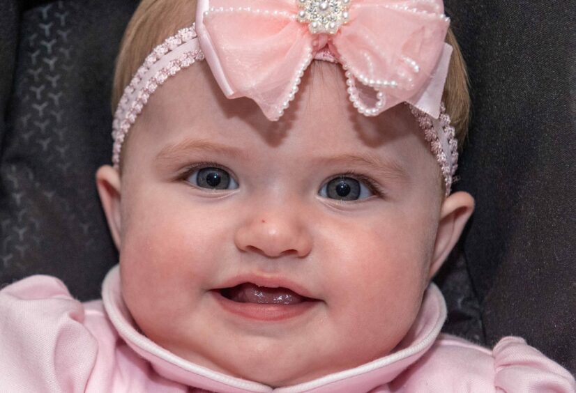 Close up of baby girl smiling with a blush pink, pearly bow.